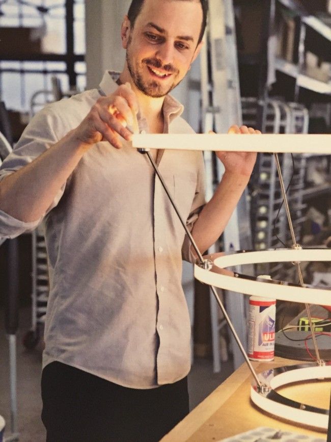 A craftsman looks over an illuminated yet partially-assembled Halo chandelier.