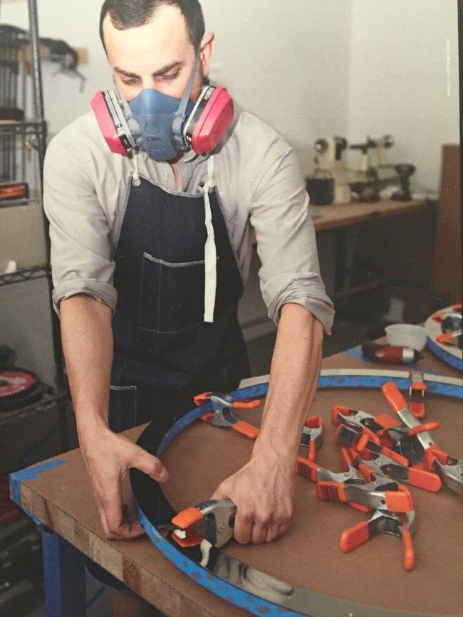 A Roll & Hill craftsman wears a breathing apparatus as he clamps together glued Halo lenses and lamping rings.