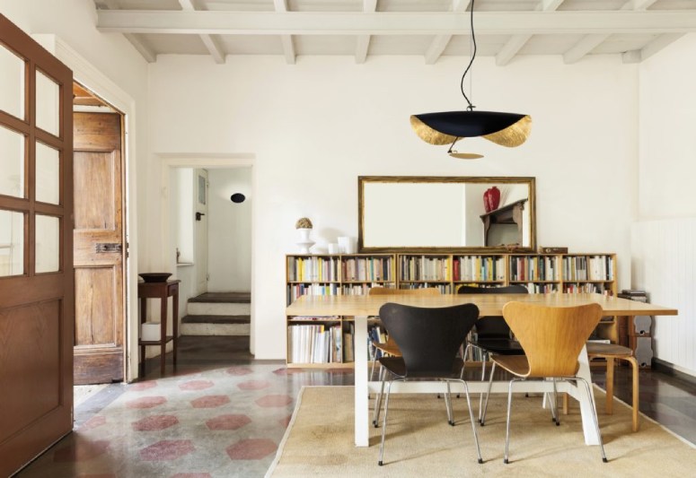 Enzo Catellani's darc awards/decorative-winning Lederam Manta S1 suspension light hangs above a wooden table in the bookshelf-lined dining area of a rustic yet luxurious home.