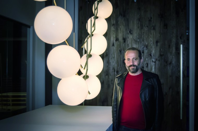 Legendary lighting designer Michael Anastassiades standing next to a linear cluster installation of his own IC Lights S pendant lights in the LightForm Toronto showroom.