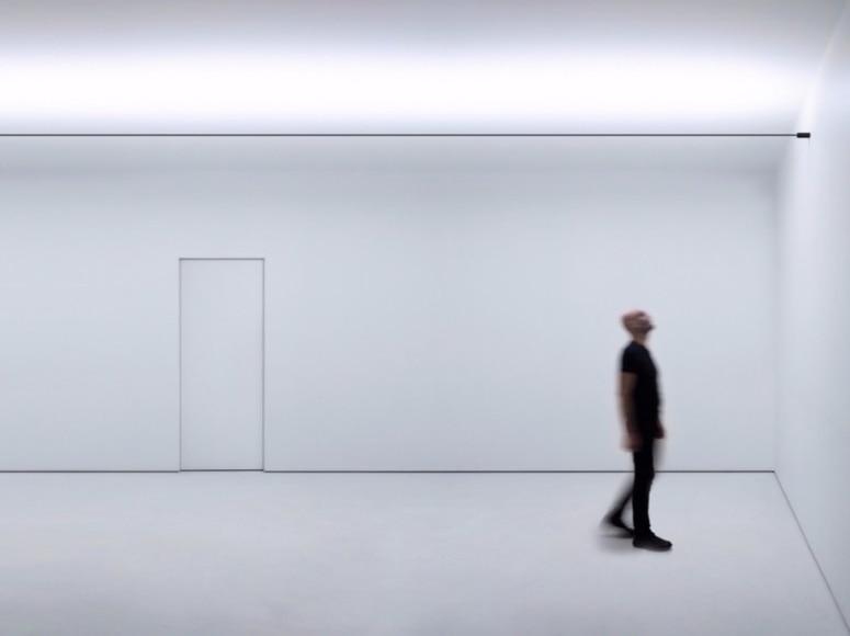 Davide Groppi's Infinito wall light cuts the space above a white room. Below, Davide Groppi makes his signature motion-blurred appearance.