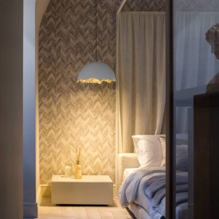 Catellani & Smith's PostKrisi suspension light hangs to the side of a comfy-looking bed.