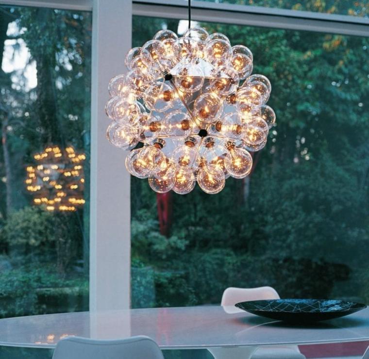 FLOS Taraxacum 88 Suspension light hangs above a dining room table, with a lush green trees visible through the glass door behind.