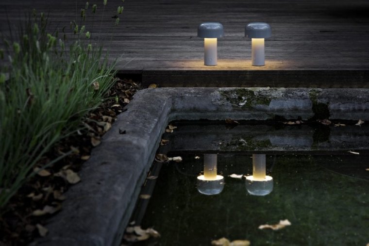 Like luminary heirs of Narcissus, two Bellhop portable table lights in grey sit on a deck bordering on a garden pond, appearing to be enraptured by their own reflections in the pond's still surface.