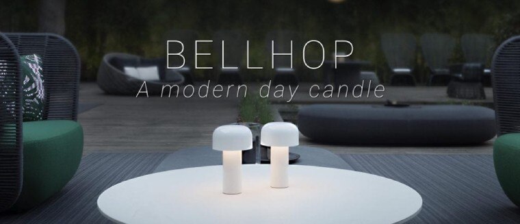 Twin FLOS Bellhop rechargeable battery operated table lights in white sit upon a patio table, surrounded by chic designer patio furniture. Text on image: BELLHOP a modern day candle