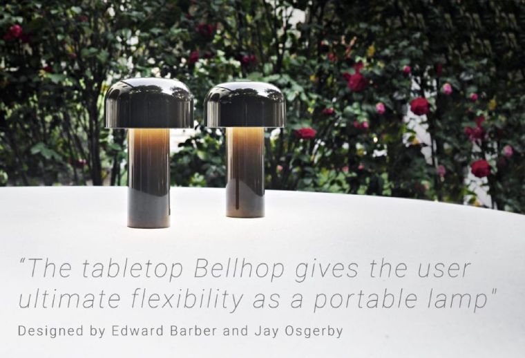 A pair of black Bellhop portable table lamps from FLOS sit on a table on a terrace. Text on image: 'The tabletop Bellhop gives the user ultimate flexibility as a portable lamp.'