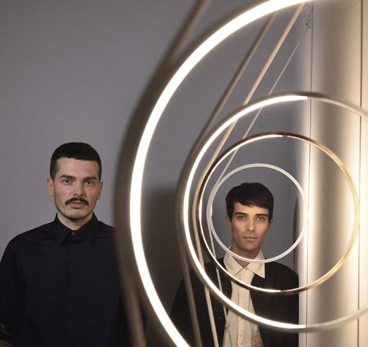 FormaFantasma's co-founders, academics, and designers Andrea Trimarchi and Simone Farresin gaze at the camera through a line of WireRing wall lights.