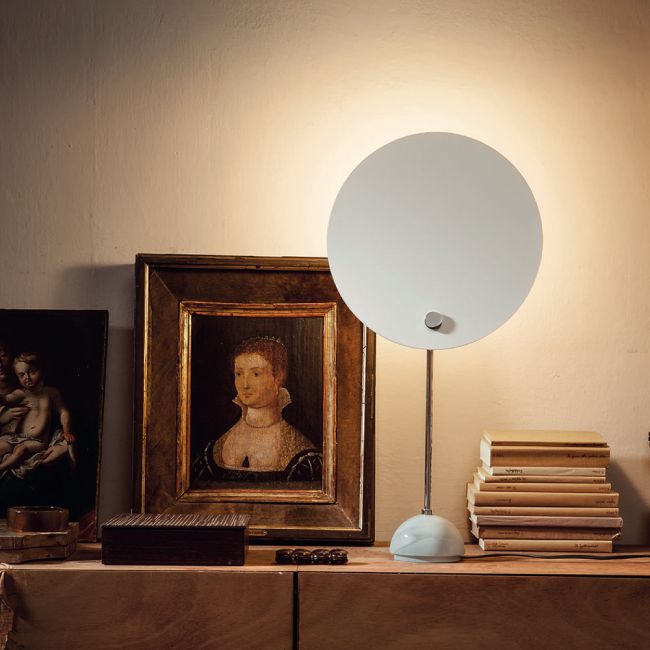 KUTA table lamp in white sits on a living credenza, casting its warm light over a stack of books and some picture frames.