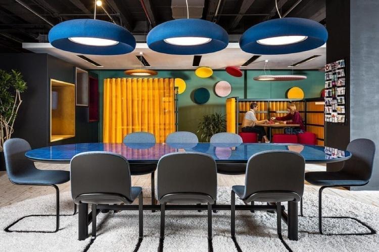 Three BuzziDome acoustic pendants hang above a blue-topped boardroom table in vibrantly-coloured in which the open concept has been compensated for with a number of sound-reduction techniques.