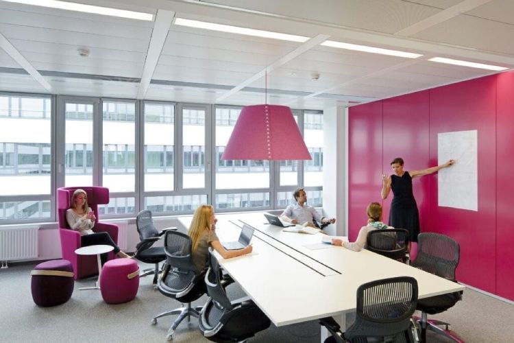 A meeting is in progress in a vibrant pink boardroom. Over the boardroom table hangs a BuzziShade XXL suspension light in pink.