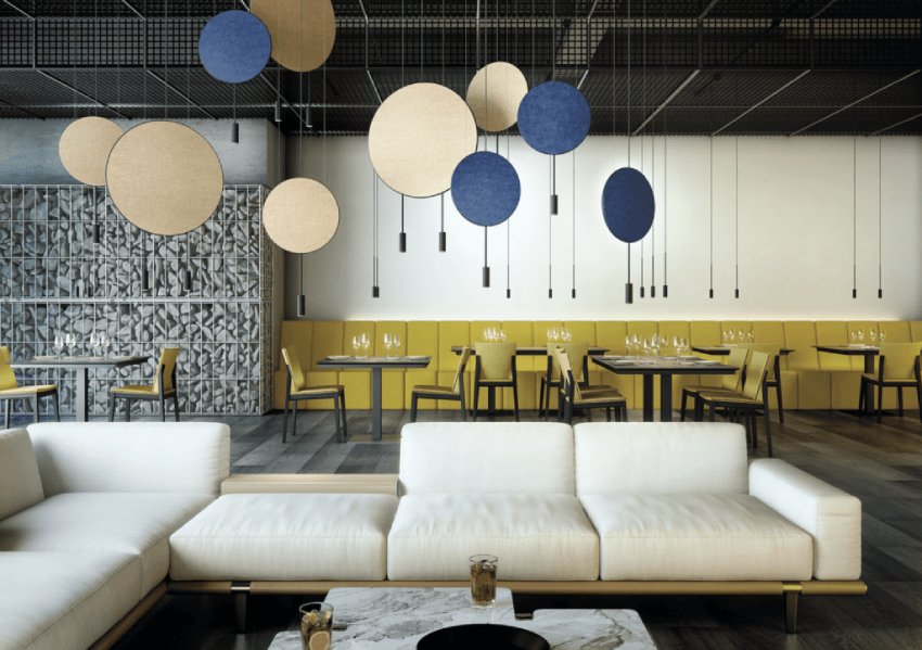 A bright, comfortable restaurant with clusters of Revolta pendant lights hanging over a central area ringed by couches. The Revolta pendants are outfitted with the optional acoustic panels to control sound.