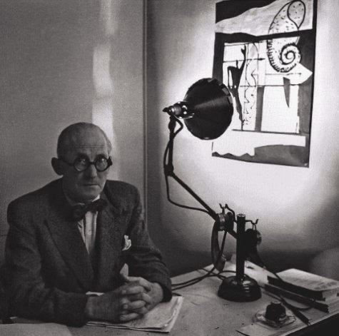 Le Corbusier sits at his desk with La Lampe Gras directed at one of his famous artworks on the wall to his side