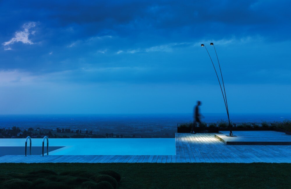 A poolside patio overlooking a valley, illuminated by Sampei Outdoor floor lamp by Enzo Calabrese and Davide Groppi.