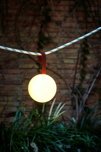 Circ M-3826X outdoor portable table light, designed by Nahtrang Studio for Estiluz, hangs from a line in a garden.