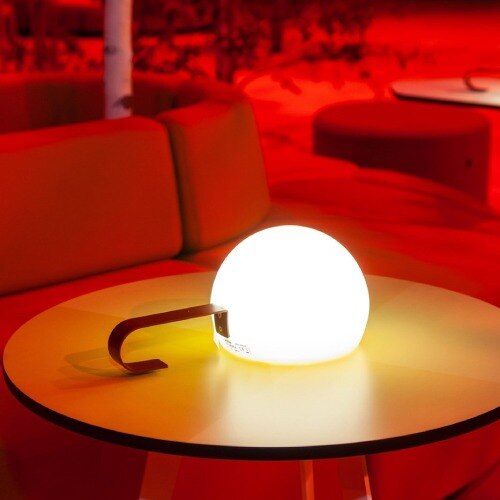 Estiluz Circ M-3826X outdoor portable table light sitting on a table on a red-tinted patio.