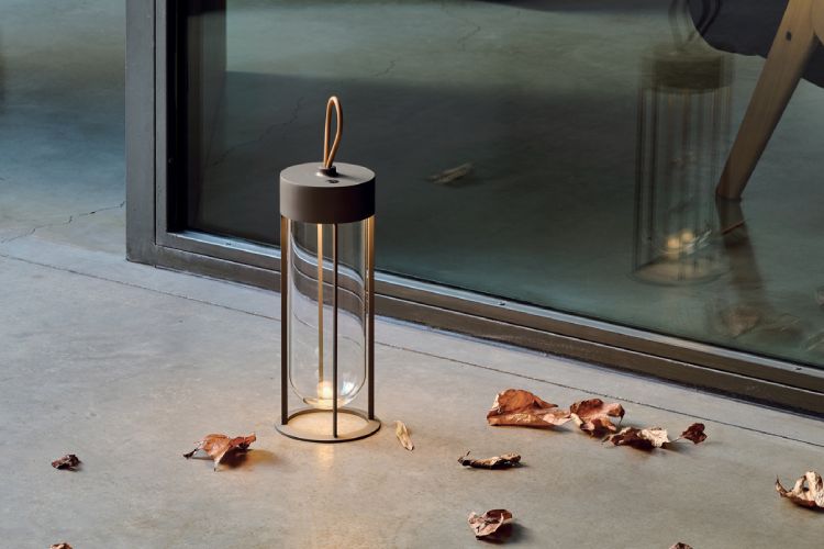 Flos' In Vitro Unplugged outdoor portable table light by Philippe Starck sits on a patio amid fallen leaves.