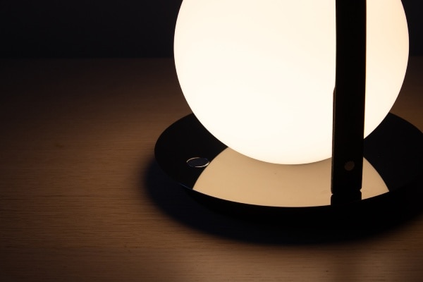 A close-up of the reflective metallic disc reflecting the illuminated opal glass globe of Bola Lantern portable table light.