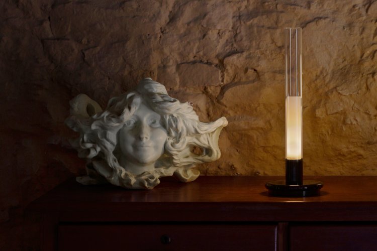 Sylvestrina portable table light from Santa & Cole sits on a sideboard next to a stone figure.