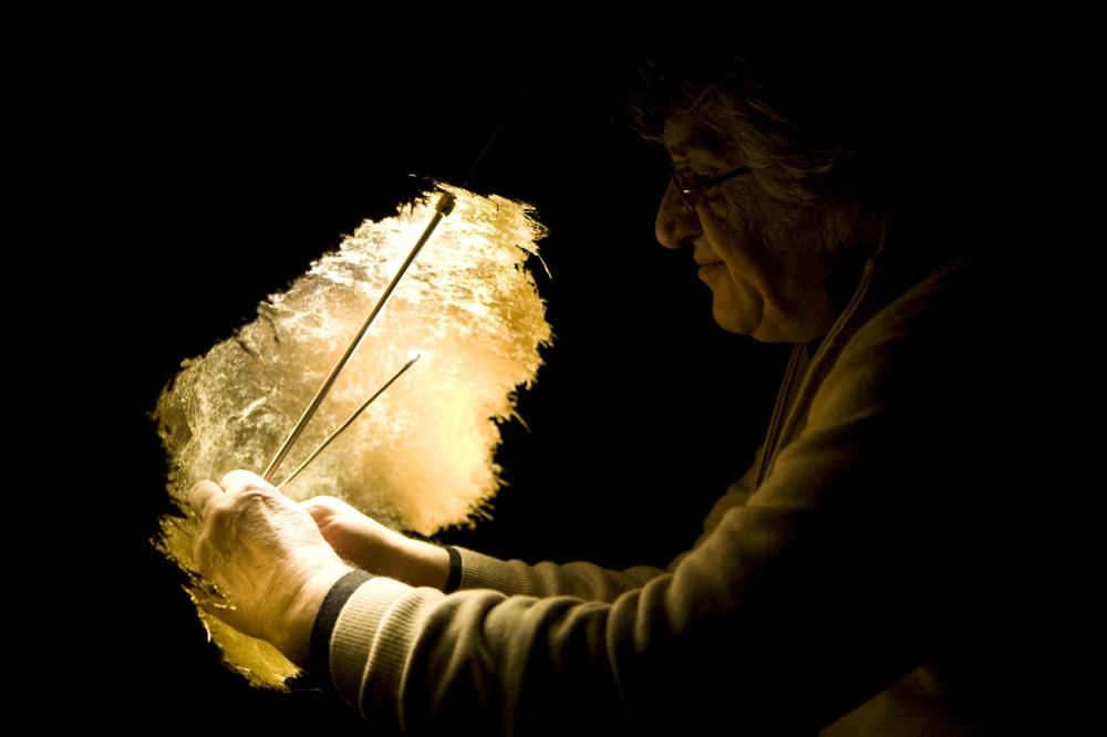 Enzo Catellani applies gold leaf to a PostKrisi 49 suspension light in a dramatically-lit shot.