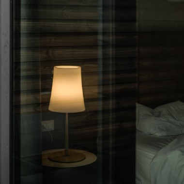 Ludovica and Roberto Palomba's Birdie Easy table light for Foscarini is seen through a sliding glass door as it illuminates the bedside of a hotel room.