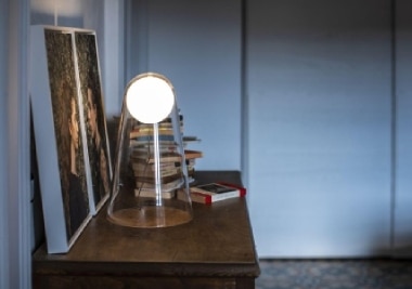 A stack of books on a side table is refracted through the cool transparent diffuser of Satellight table lamp, designed by Eugeni Quitllet.