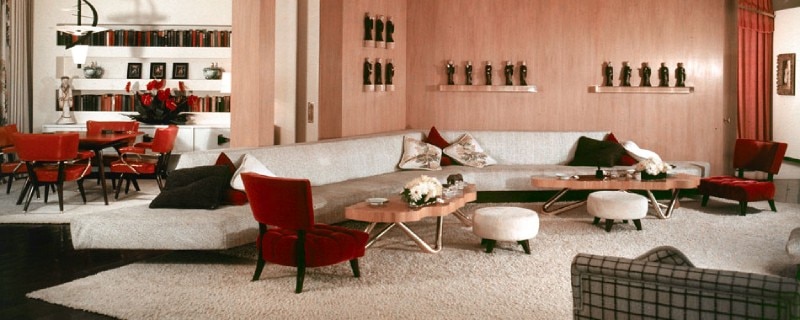 A California Modern home designed by Billy Haines and featuring many of his furniture designs. Open concept, the dining room and living room are divided by a short wall. The colour scheme is reds, pinks, whites, and greys.