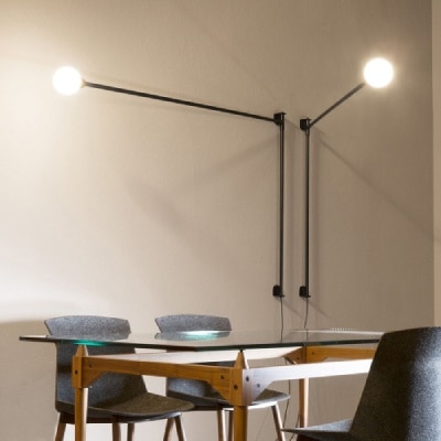 A pair of Charlotte Perriand's Pivotante À Poser wall lights swing their arms out over a glass-top table surrounded by dining room chairs.