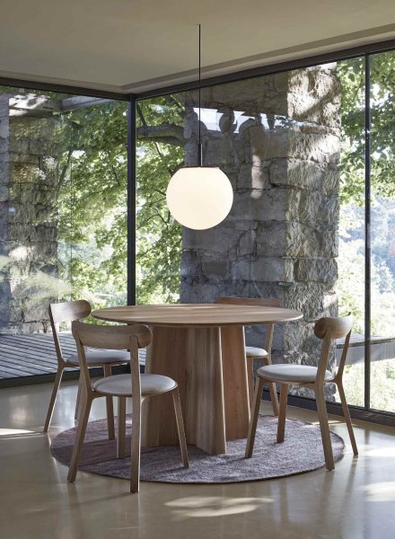 Sfera suspension light, designed for Brokis by creative director Lucie Koldova, hangs above a simple dining table in a glass-walled dining area overlooking lush wilderness.