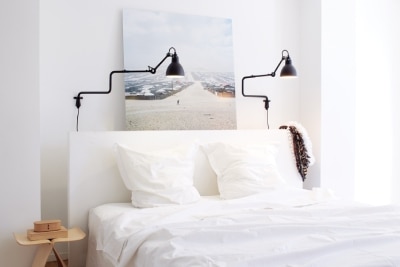 A pair of La Lampe Gras wall lights from DCWéditions illuminate a bedroom.