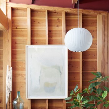 Herman Miller's Nelson Bubble Ball pendant hangs in front of an exposed wood wall on which hangs a painting.