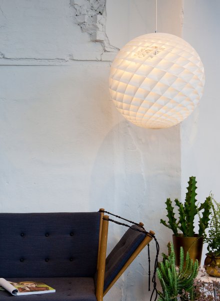 Patera pendant light in the 60cm size hangs over the arm of a couch with a fold-out magazine holder. Designed for Louis Poulsen by Oivind Slaatto.