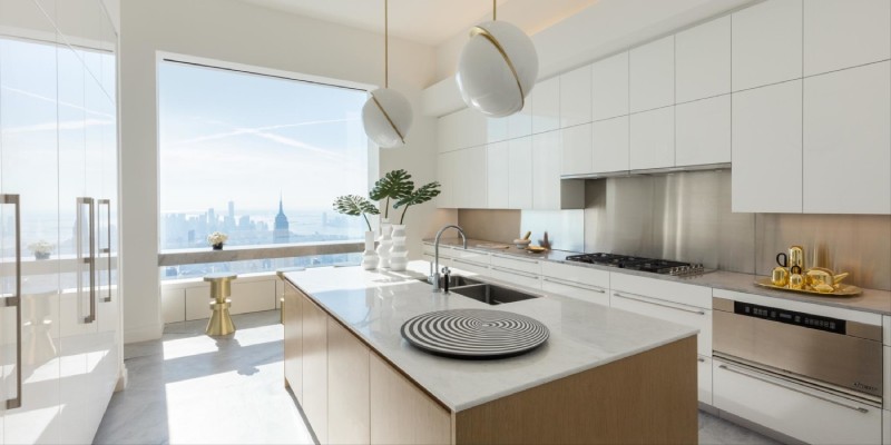 A New York high rise apartment kitchen with a pair of Lee Broom's Crescent pendant lights over the kitchen island. A bay window reveals the New York City skyline in the background.