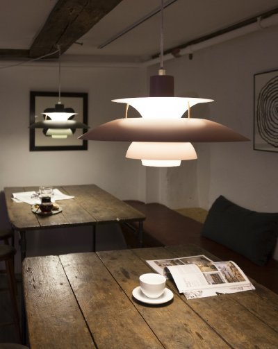 PH 5 pendant light, designed by Poul Henningsen for Louis Poulsen, hang over rustic wooden tables in a dramatically-lit restaurant.