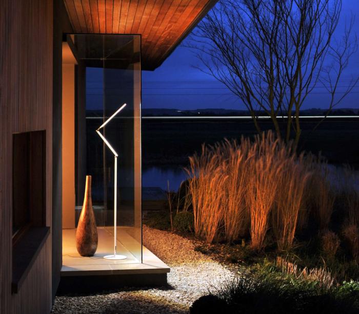 Z-Bar floor light looks through a glass wall to illuminate a lush exterior.