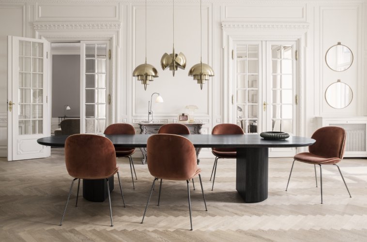 A trio of brass-finished Multi-Lites from Gubi hang in a line over a black table in a luxuriously spacious dining room. BestLite BL1 table light and BestLite BL2 Desk Lamp by Robert Dudley Best are also visible in the background.