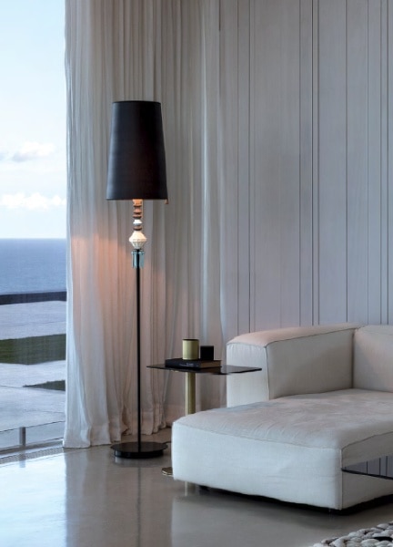 A Belle de Nuit floor lamp stands next to the patio door of a luxurious hotel room.