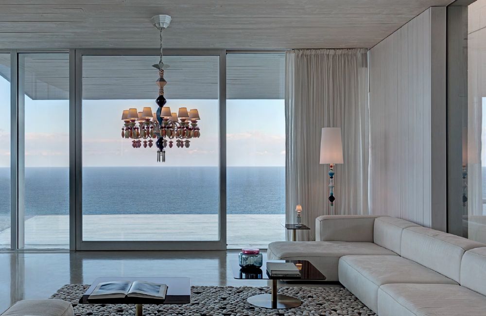 Belle de Nuit 12 chandelier and Belle de Nuit floor lamp illuminate a chic modern living room overlooking the ocean through glass patio doors.