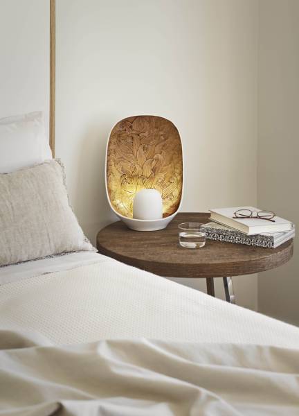 A Mirage table lamp from Lladro on a night stand next to a bed.