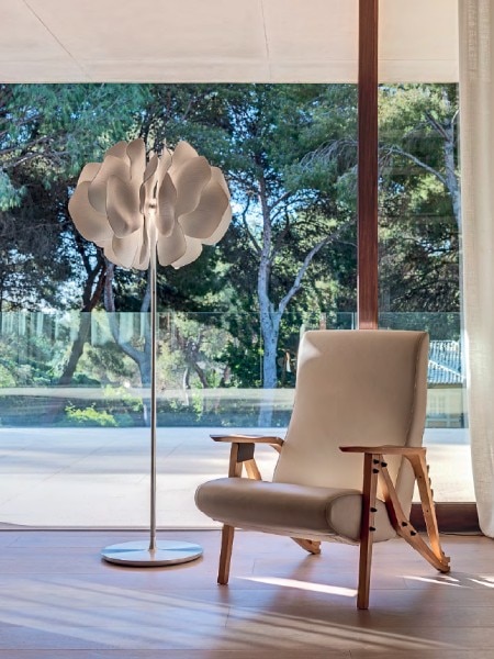 A Nightbloom floor lamp in a mid-century modern living room overlooking a pool deck through a patio door.