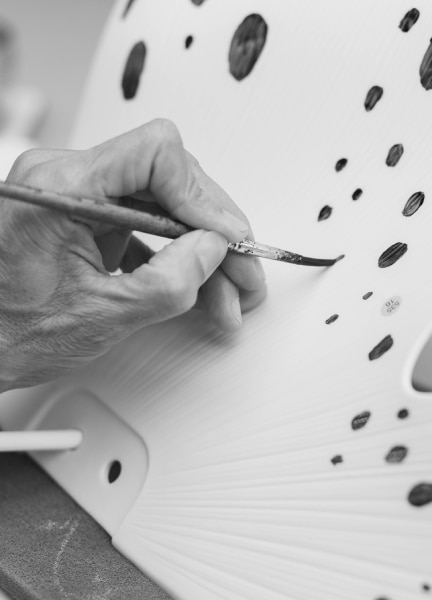 A b&w close-up of the hand of a Lladro artisan applying gold glaze to a porcelain Nightbloom petal