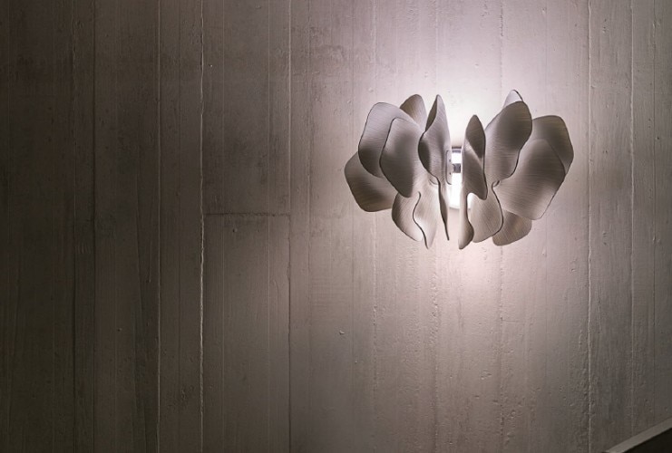 Nightbloom wall sconce illuminates a rustic painted wall.