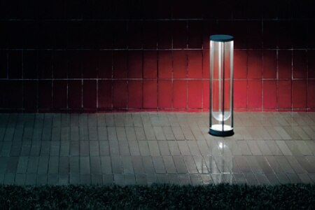 A moody outdoor shot of In Vitro Outdoor Bollard floor light, designed for Flos by Philippe Starck, installed in a tiled walkway.