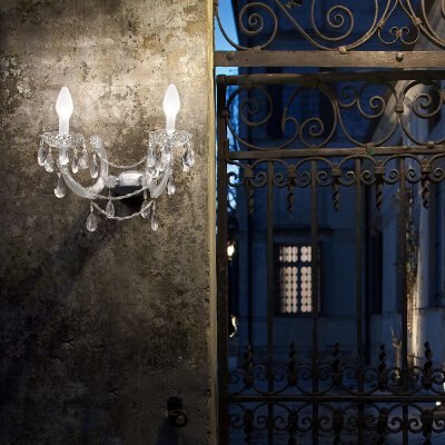 Dryligh A2 outdoor wall sconce on a weathered cement wall next to an intricate wrought iron gate.