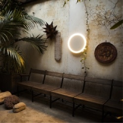 Amigo wall sconce from Santa & Cole over a bench in a rustic garden.