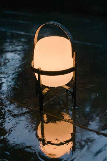 The durable Cestita Alubat outdoor table light glows gorgeously amid falling rain.