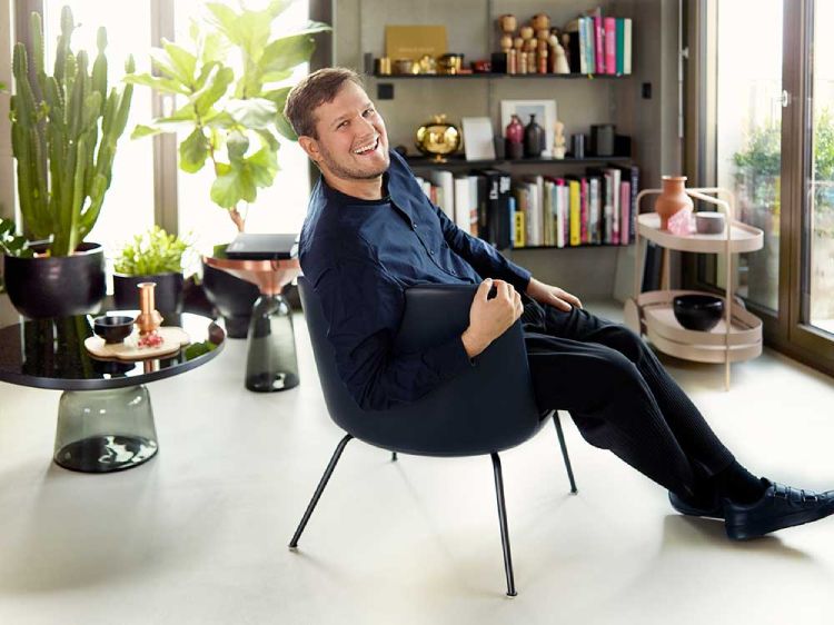 Designer Sebastian Herkner reclines in a chair with his Bell tables in the background.