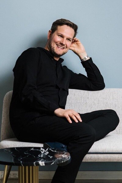 Lighting Designer Sebastian Herkner smiles on a sofa.