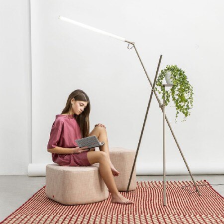 A woman reads beneath the light of Asana-3768 from Estiluz, which also provides a surface for a plant to rest upon.