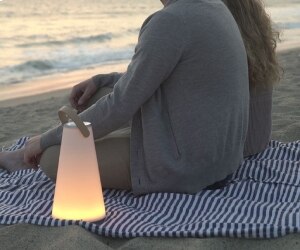 Carmine Deganello's Uma portable table lamp from Pablo sits on a beach blanket next to a couple enjoying a sunset.