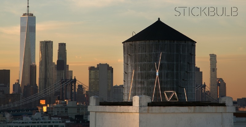 The New York City skyline, with a classic water tower foregrounded. Around the water tower stand Stickbulb luminaires.